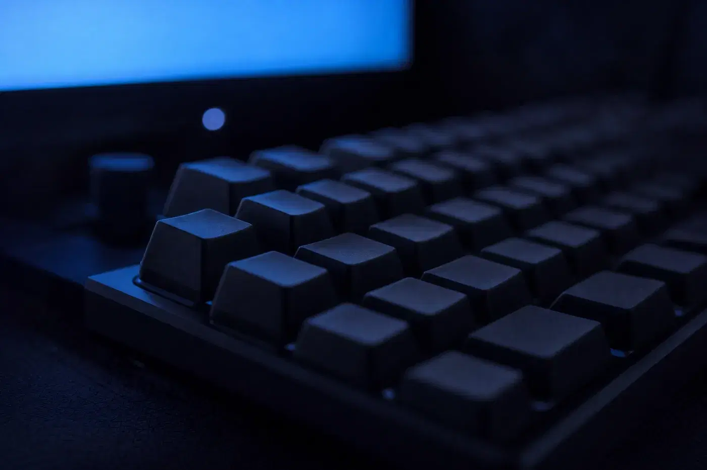 Teclado mecánico oscuro iluminado por el brillo azul de un monitor